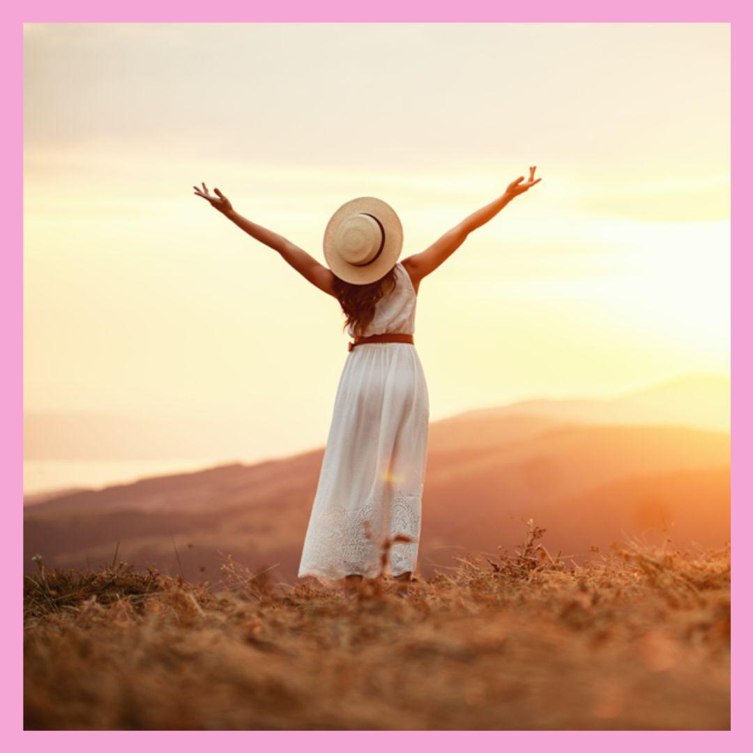Femme debout dans un paysage naturel, bras levés, tournée vers l’horizon